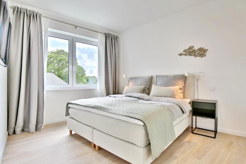 A modern bedroom with a large bed, a bedside table, and a window with curtains.