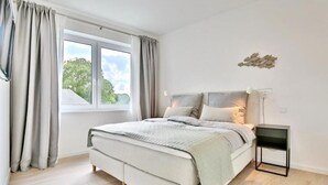 Ein modernes Schlafzimmer mit einem großen Bett, einem Nachttisch und einem Fenster mit Vorhängen.