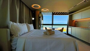 Ein Hotelzimmer mit einem großen Bett, Meerblick und einer Essecke mit Tisch und Stühlen.