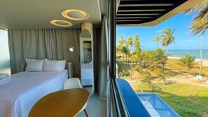 Ein Hotelzimmer mit Bett, Sessel, Balkon und Blick auf Strand und Palmen.