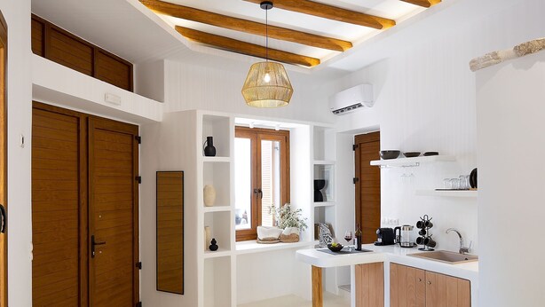 Ett modernt hotellrum med en öppen sovplats på ett loft, ett litet kök och ett stort fönster som släpper in naturligt ljus.