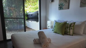 A neatly made bed with a rolled towel, a nightstand with a lamp, and a view of greenery outside. - 2 Bedroom Pool Apartment (Las Terrenas)