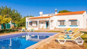 Un espace aménagé au bord de la piscine, comprenant une piscine, des chaises longues et un bâtiment blanc doté d’un toit en tuiles.