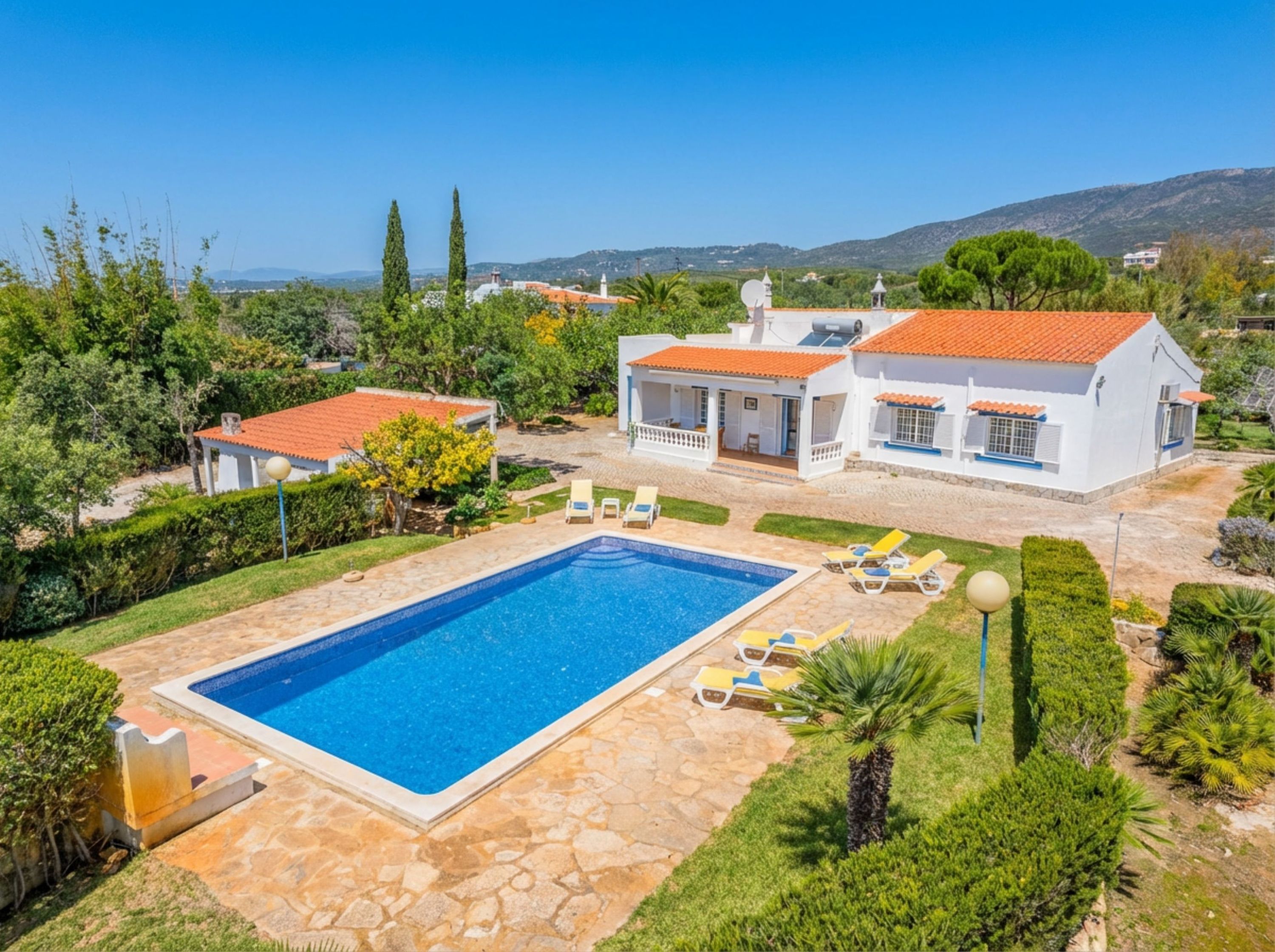 A villa with a swimming pool, outdoor seating, and a view of the surrounding landscape.