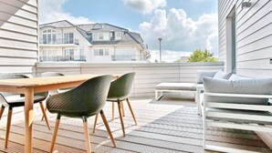 Una terrassa de fusta amb taula i cadires, un sofà i vista d'un edifici de dues plantes.