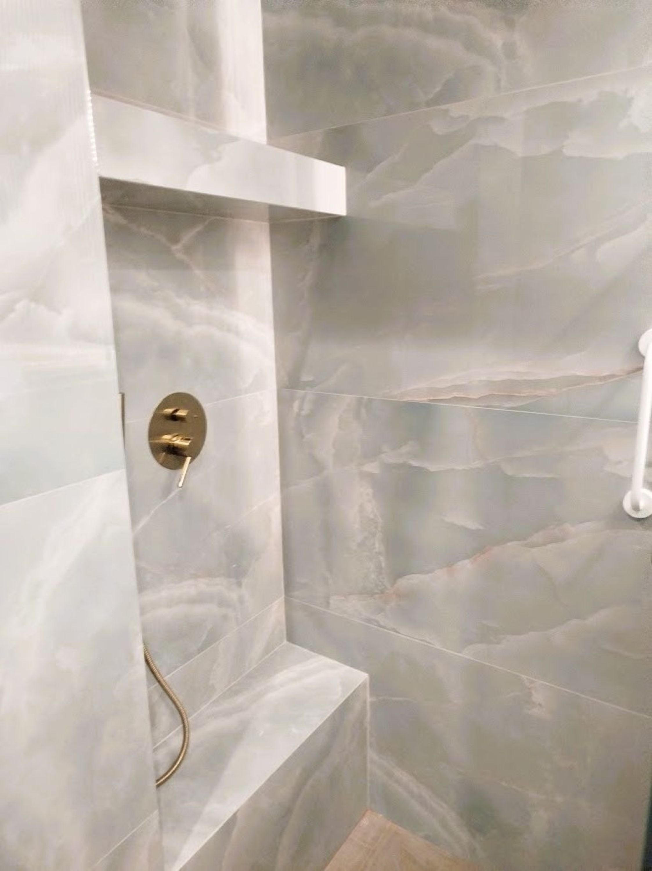 A bathroom with a marble shower wall and a gold shower control.