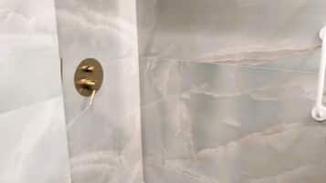 A bathroom with a marble shower wall and a gold shower control.