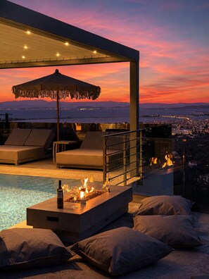 Un espace piscine aménagé sur le toit, avec des chaises longues, un foyer et une vue sur la ville au coucher du soleil.