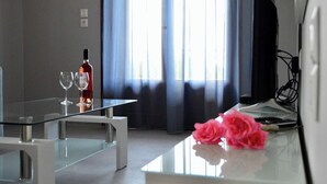 A modern hotel room with a glass table, a bottle of red wine, two wine glasses, and a pink rose on the table.