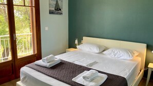 A hotel room with a bed, two pillows, a bedside table with a lamp, a window with a view of trees, and an air conditioning unit on the wall.
