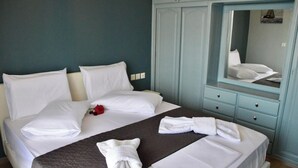 A neatly made bed with white linens and a dark brown bedspread, a mirror above the bed, and a light blue wardrobe with a mirror.