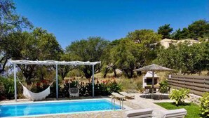 A swimming pool with a pergola, lounge chairs, and a small gazebo.