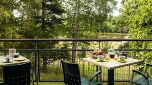 En terrasse med et bord dækket til morgenmad, med udsigt over en sø omgivet af træer.