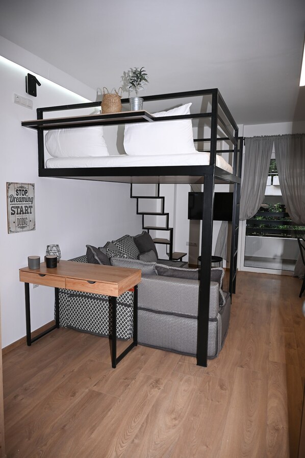 Ein Etagenbett mit Schreibtisch und Stauraum, einem Fernseher und einer Treppe, die zu einem Balkon mit Pflanzen führt.