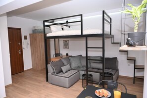 Ein gemütlicher Raum mit Etagenbett, einer Couch, einem Esstisch mit Essen und einem Glas Orangensaft sowie einer kleinen Pflanze auf einem Regal.