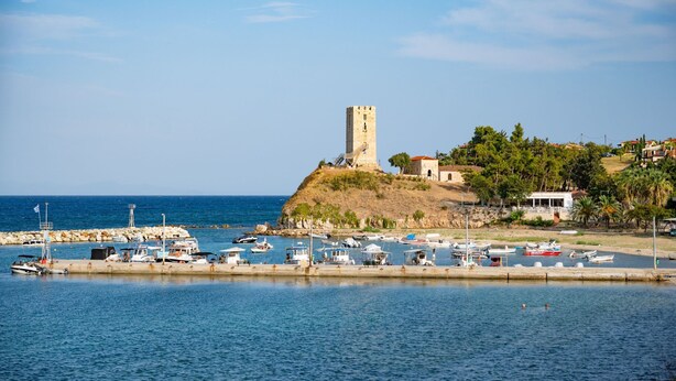 A coastal town with a prominent tower on a hill, a marina with various boats, and a clear blue sky. - Sunny Villa Tessera in Chaniotis (Chaniotis)