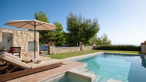 A swimming pool with a stone wall, a lounge chair, and an umbrella. - Sunny Villa Tessera in Chaniotis (Chaniotis)