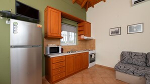 Eine kleine Küche mit Holdekor-Schränken, einem Edelstahl-Kühlschrank, einer Mikrowelle und einem Herd. Ein Fenster bietet Blick ins Freie, und in der Ecke steht eine Couch.
