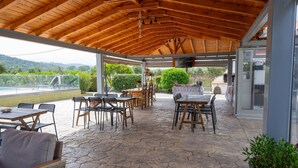 An outdoor patio with stone flooring, wooden tables and chairs, a TV, and a view of the countryside. - Τριαντάφυλλο/Rose near to sea with heating pool (Mavrovouni)