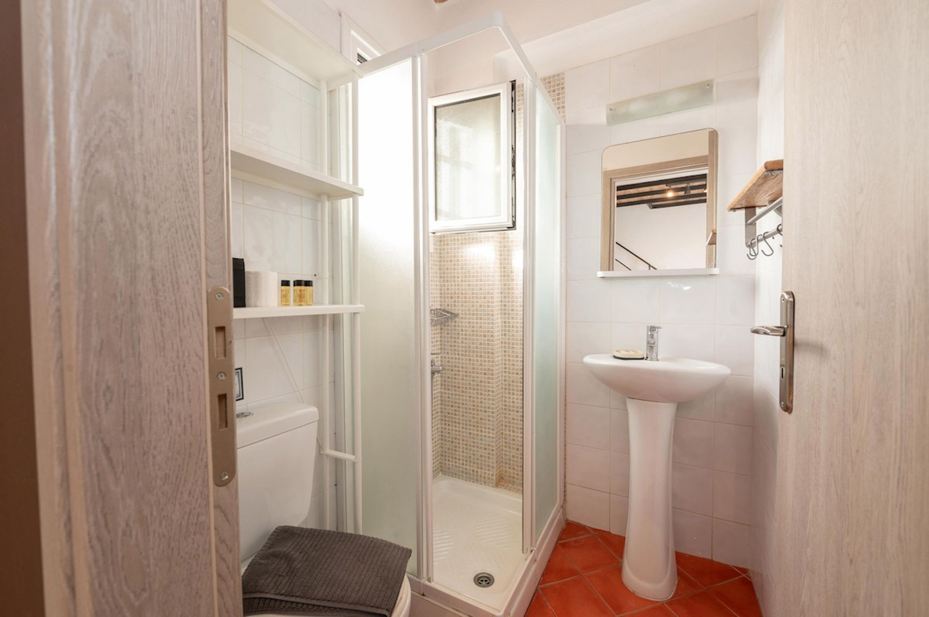 Un baño con ducha de vidrio, lavamanos pedestal y suelo de baldosas.