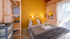 Quarto com teto de madeira, cama com almofadas brancas e mostarda, mesa de cabeceira com controle remoto e janela com cortinas.