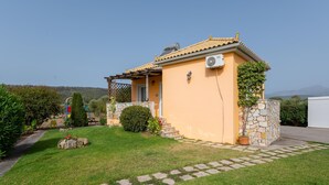 Une petite maison avec un mur en pierre, un toit en tuiles et un jardin avec un chemin menant à l’entrée.