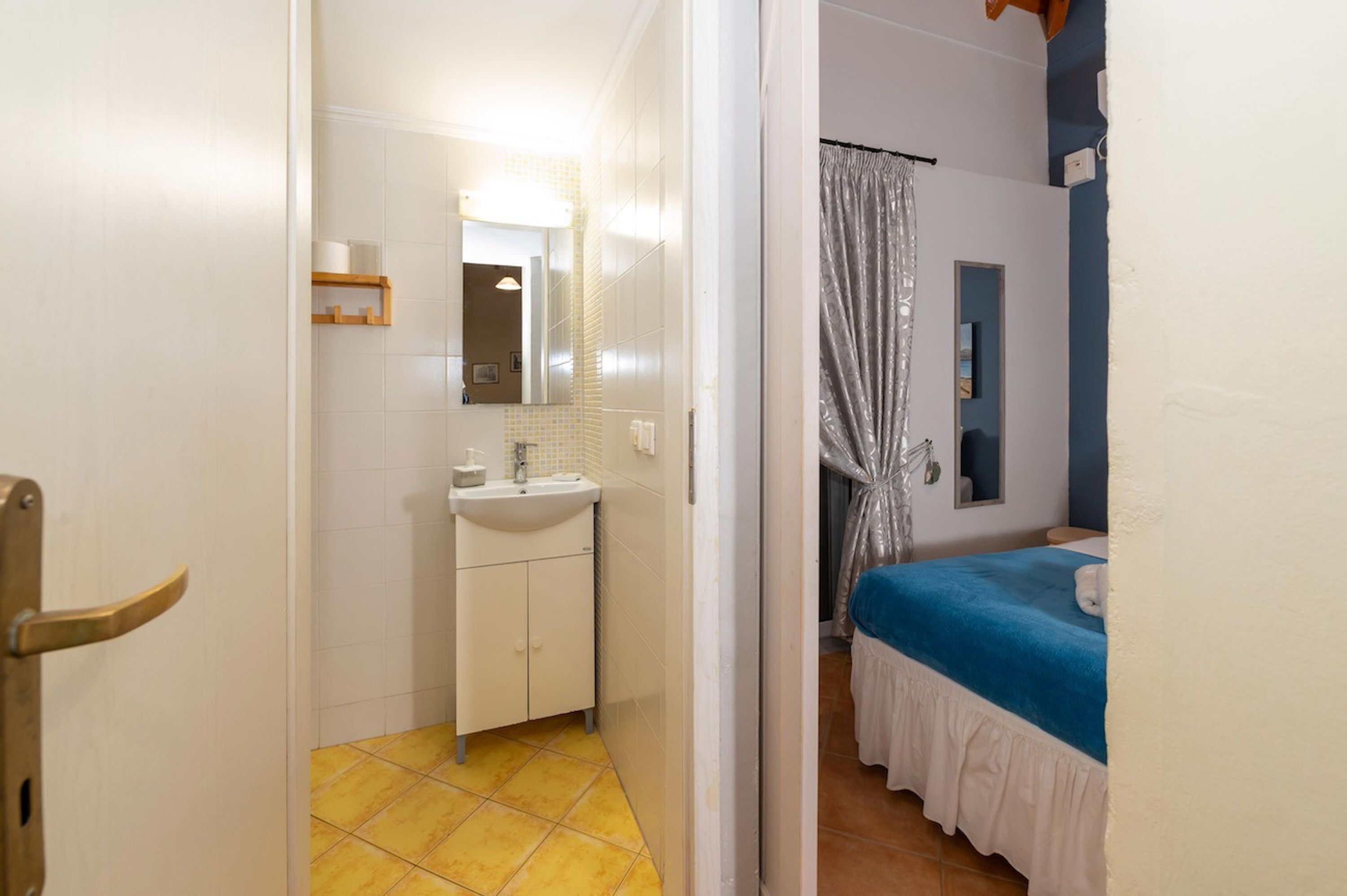 A bathroom with a sink, mirror, and yellow-tiled floor.