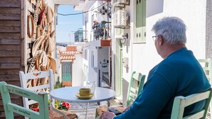 Un homme est assis à une table, devant une tasse et une soucoupe, entouré de chaises en osier et d’une petite table.