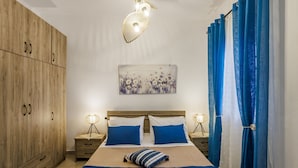 Une chambre à coucher avec un lit, une armoire en bois, deux tables de chevet avec des lampes, un tableau au mur et des rideaux bleus.