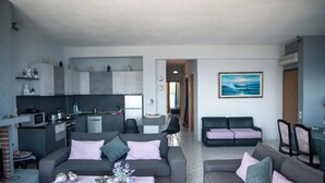 Una sala moderna con sofás grises, una mesita de centro y una cocina al fondo.