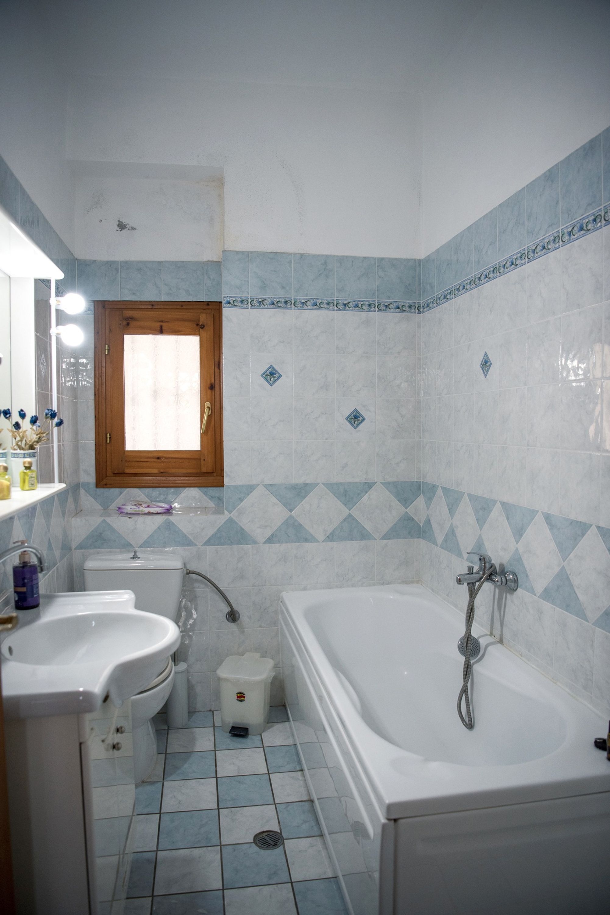 A bathroom with a sink, toilet, and bathtub, featuring blue and white tiles and a wooden window.