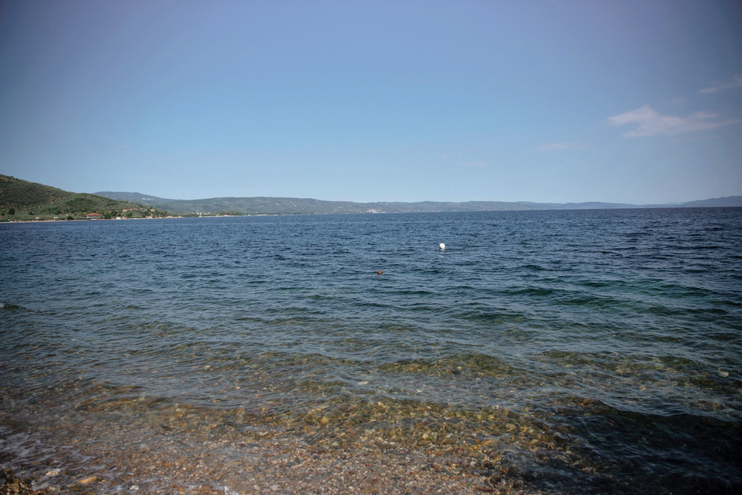 A clear view of a lake with a shoreline and distant hills.