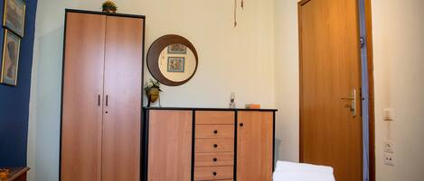 A bedroom with a bed, a wooden wardrobe, a mirror, and a door.