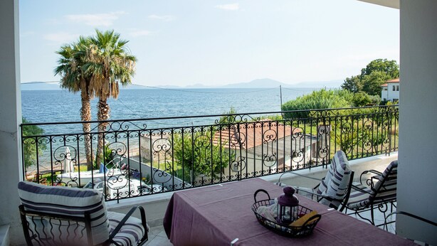 Un balcón con mesa lista para comer, con vista al mar, una palmera y un cielo despejado.