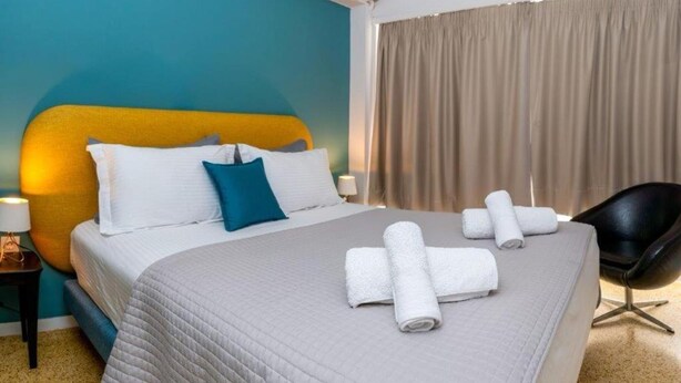 A hotel room with a large bed, a headboard, a nightstand, a lamp, a chair, and a window with curtains. - Crown Syntagma Apartment (Athina)