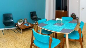A conference room with a round table, blue chairs, a wooden cabinet, and a small plant on a side table. - Crown Syntagma Apartment (Athina)