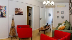 A living room with red chairs, a green sofa, a coffee table, and artwork on the walls. - Crown Syntagma Apartment (Athina)
