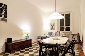 Un comedor con una mesa redonda, sillas, una lámpara, un radiador y una ventana.