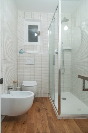 Un baño moderno con cabina de ducha de vidrio, un lavabo blanco y un inodoro.
