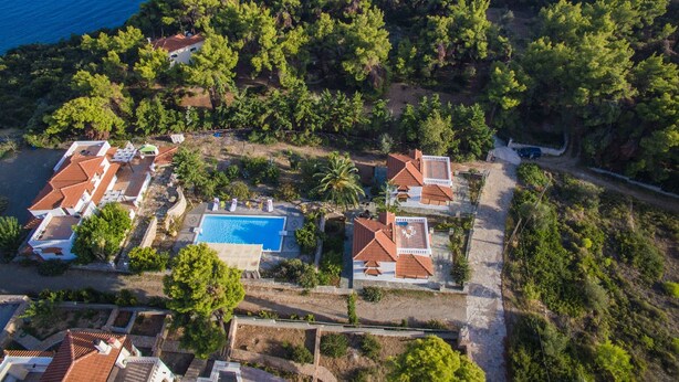 Vista aérea de uma propriedade costeira com várias villas, uma piscina e vegetação exuberante.