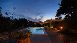 A swimming pool with a pergola and chairs, surrounded by plants and a stone wall. - Kamelia Villa 3 in Alonissos (Votsi)