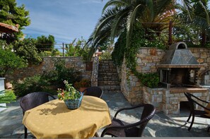 Eine Terrasse im Freien mit Steinmauern, einem Grill aus Ziegeln, Korbstühlen und einem Tisch mit gelber Tischdecke.