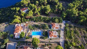 Vista aérea de uma propriedade costeira com vários edifícios, piscina e vegetação exuberante.