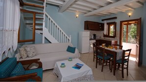 Uma sala de estar acolhedora com sofá, uma mesa de jantar com cadeiras, uma cozinha com frigorífico e uma escada.