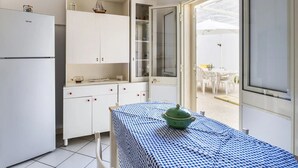 A compact kitchen with white cabinets, a small table with a blue and white checkered tablecloth, and a green pot on the table. - Villa del Cortile Ionico (Porto Cesareo)