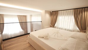 A hotel room with a large bed, beige curtains, and a wooden floor.