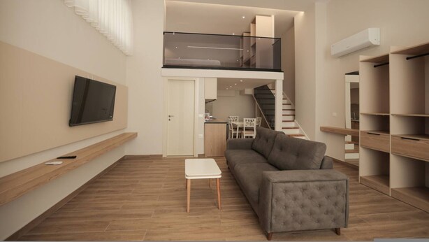 A modern living room with a grey sofa, a small white table, and a TV mounted on the wall.