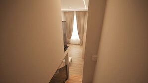 A staircase leading to a room with a wooden floor and a view of a window with curtains. - Duplex City 05 in Durrës (Durrës)