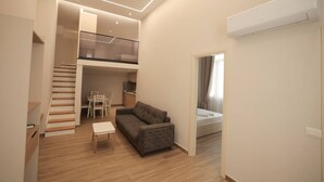 A modern apartment with a staircase leading to a loft, a living area with a sofa and table, and a kitchenette. - Duplex City 05 in Durrës (Durrës)