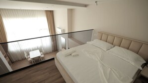 Quarto de hotel moderno com uma cama grande, varanda de vidro e uma pequena área de trabalho.